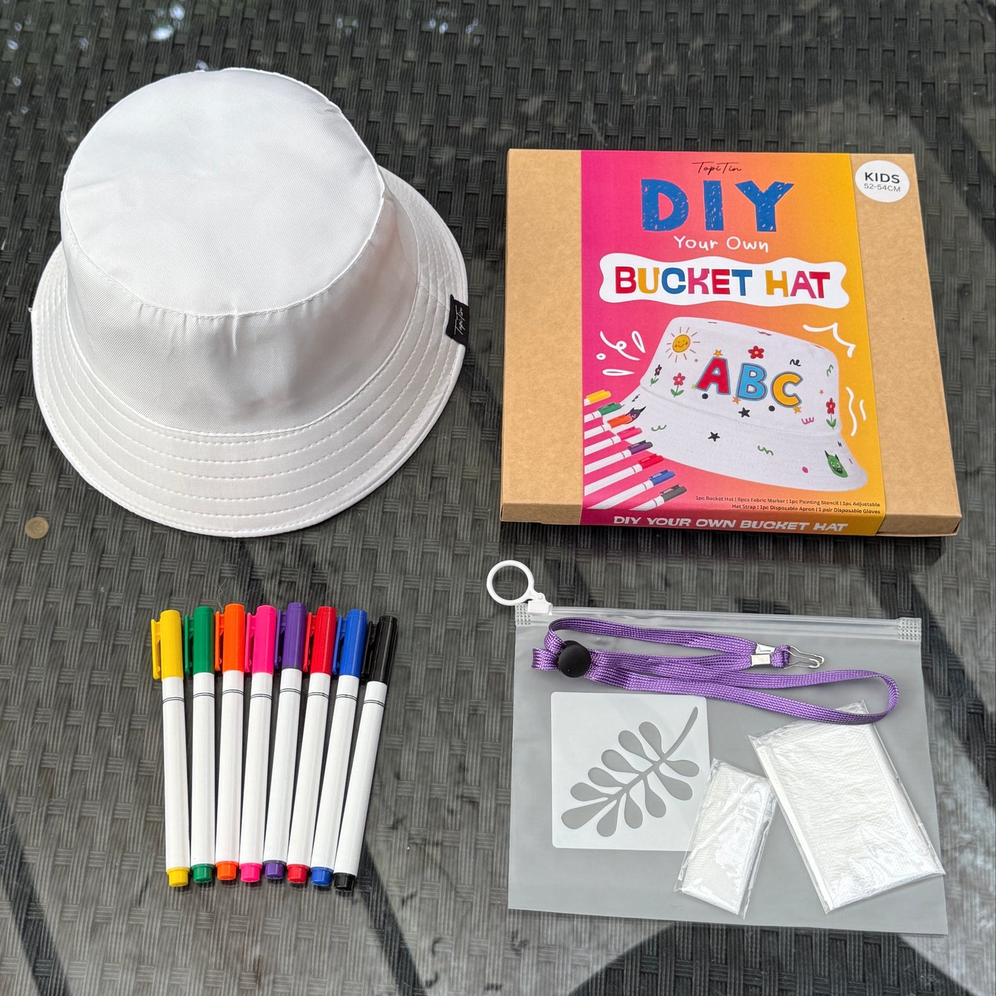 White bucket hat, DIY kit box, markers, and stencils on a glass table.